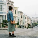 Woman wearing a layered San Francisco outfit idea with a denim jacket and ankle boots in front of the Painted Ladies
